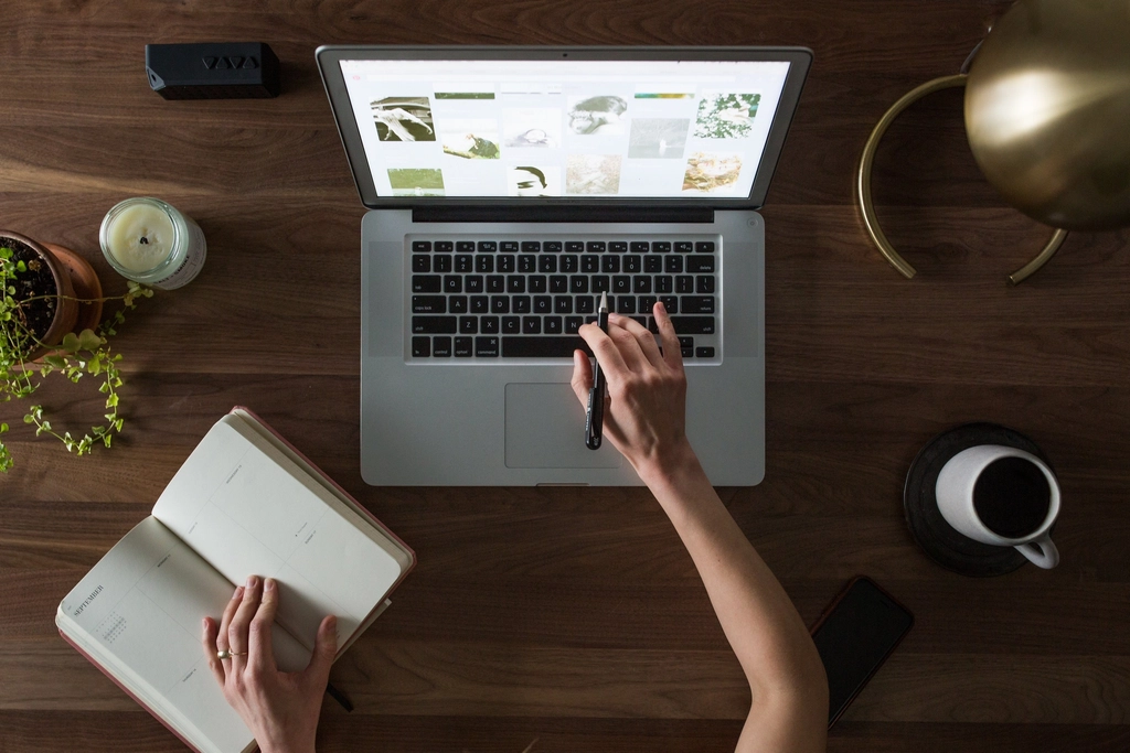 Handen met een koffiekop naast een laptop op een bureau